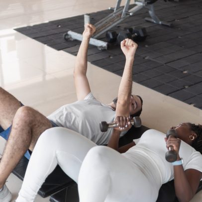 Interracial couple lifting weights while lying on gym floor, strengthening their muscles and improving fitness